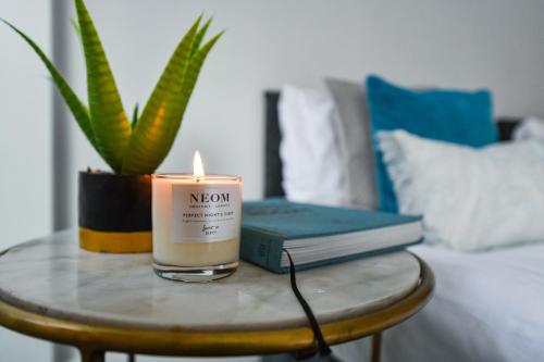a candle on a table with a book and a plant at Long Eaton Modern 4bed House in Long Eaton