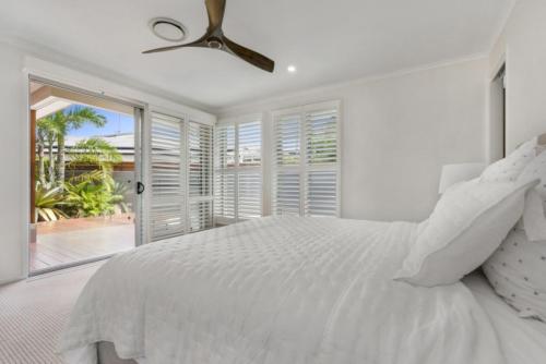 biała sypialnia z łóżkiem i wentylatorem sufitowym w obiekcie Key Ct 10 w mieście Noosa Heads
