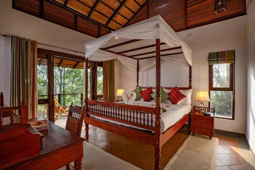 a bedroom with a canopy bed with a desk and windows at Vythiri Mist Resort in Vythiri