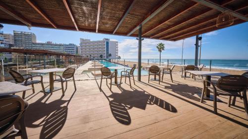 a patio with tables and chairs on the beach at Cádiz Bahía by QHotels in Cádiz