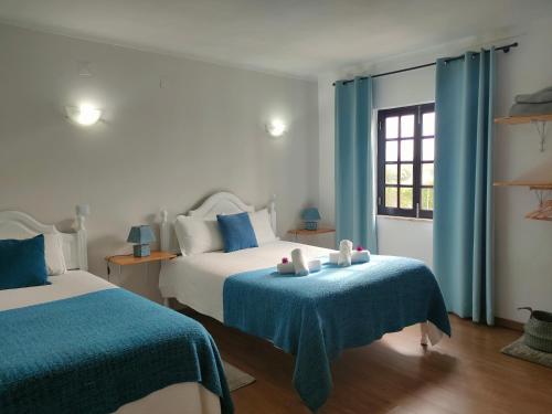 a bedroom with two beds and a window with blue curtains at Vicentina Rooms by Casas do Alentejo in Almograve