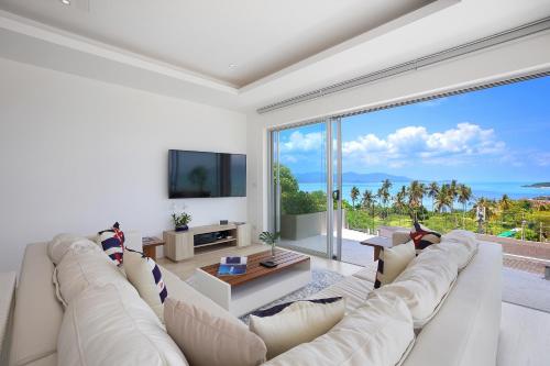 a living room with a white couch and a large window at Samui Bayside Luxury Villas in Choeng Mon Beach