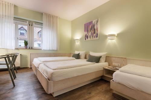 Un dormitorio con dos camas y una mesa y dos ventanas. en Hotel Kunterbunt in Würzburger Innenstadt, en Würzburg