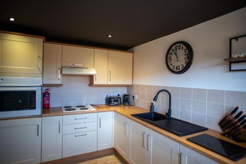 a kitchen with white cabinets and a clock on the wall at The Stables - Quirky one bed holiday home with wood fired hot tub in Rudston