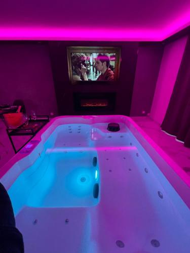 uma banheira num quarto com luzes cor-de-rosa em Suite cinéma et jacuzzi privé em Melun