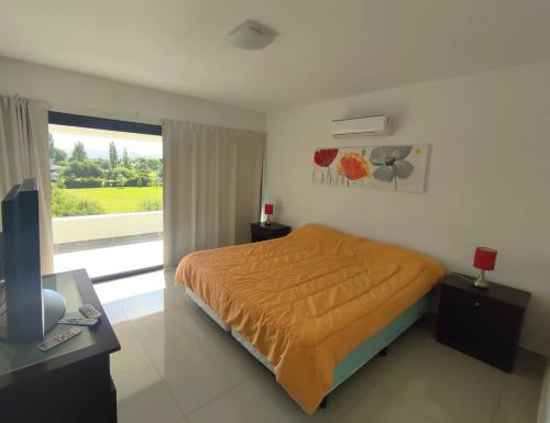 1 dormitorio con cama con colcha de color naranja y ventana en Casa Carlos Paz en Country Causana en Villa Carlos Paz