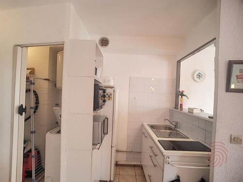 La cuisine blanche est équipée d'un évier et d'un réfrigérateur. dans l'établissement Appartement F2 lumineux avec balcon, proche centre et Thermes, animaux acceptés, wifi gratuit - FR-1-451-21, à Lamalou-les-Bains