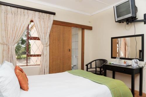 a bedroom with a bed and a desk and a television at Bisho Park guesthouse in King Williamʼs Town