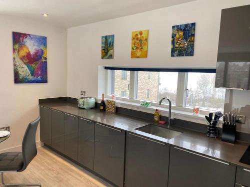a kitchen with stainless steel appliances and paintings on the wall at Exquisite & Contemporary 2 Bed Apartment w Parking 10 mins walk to Papworth, Addenbrookes hospitals & Bio Medical Campus in Trumpington