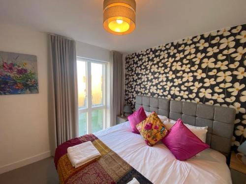 a bedroom with a bed with pink pillows and a window at Exquisite & Contemporary 2 Bed Apartment w Parking 10 mins walk to Papworth, Addenbrookes hospitals & Bio Medical Campus in Trumpington