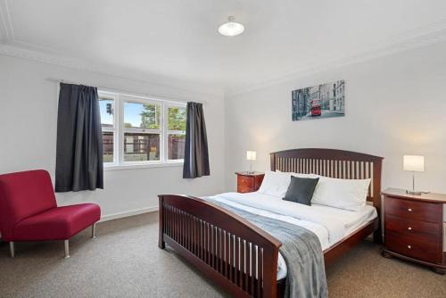 ein Schlafzimmer mit einem Bett und einem roten Stuhl in der Unterkunft Homey Hideaway 3 BR w Parking , Wi-fi and Netflix in Auckland
