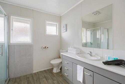 ein Badezimmer mit einem Waschbecken, einem WC und einem Spiegel in der Unterkunft Homey Hideaway 3 BR w Parking , Wi-fi and Netflix in Auckland