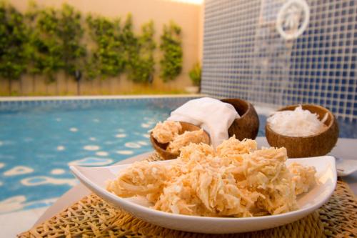Casa de Praia Pouso das Fadas com Arrumadeira e Equipe de Cozinha في ماراغوغي: طبق من الطعام على طاولة بجوار حمام سباحة