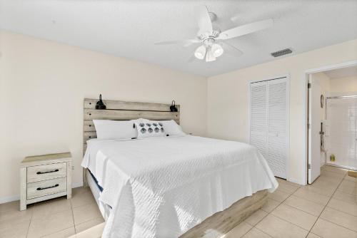 a white bedroom with a bed and a ceiling fan at Oceanview Haven - 2BR Beach House with Patio Heated Pool Steps from Paradise Beach Park! in Melbourne