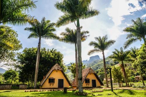 a house with palm trees and mountains in the background at Villa das Palmeiras Chalés & Camping in São Bento do Sapucaí