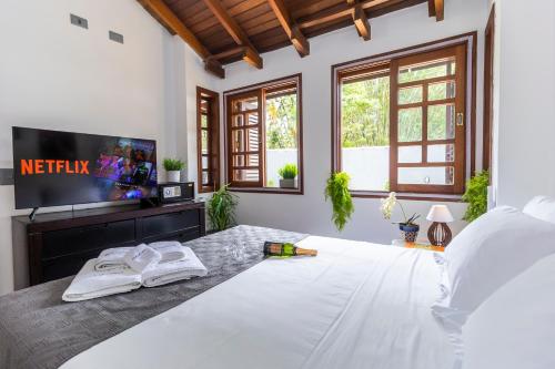 um quarto com uma grande cama branca e uma televisão de ecrã plano em Casa Charmosa com Piscina em Barra do Una em Barra do Una