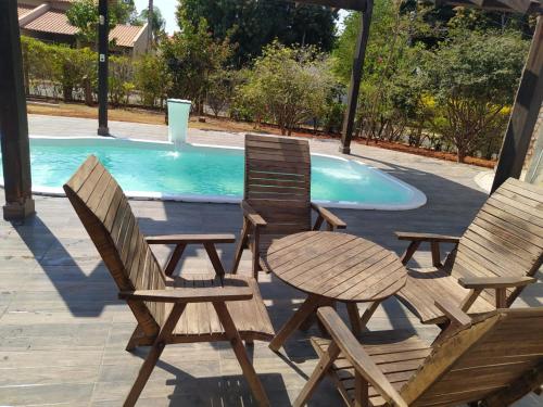 3 sillas de madera y una mesa junto a la piscina en Casa em Caldas - PISCINA SOLAR E ELETRICA, en Caldas Novas