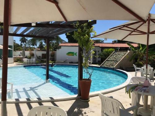 a swimming pool with an umbrella and chairs at Mandakaru Residence Flat da Isa 01 in Porto De Galinhas