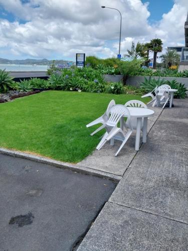two white chairs and a table and a grass field at Bayview Motel in Paihia