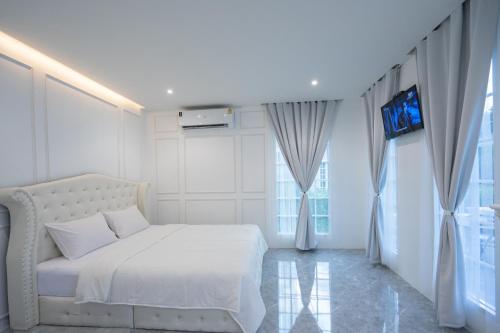 a white bedroom with a white bed and a tv at Je t'aime cafe & villa in Sing Buri