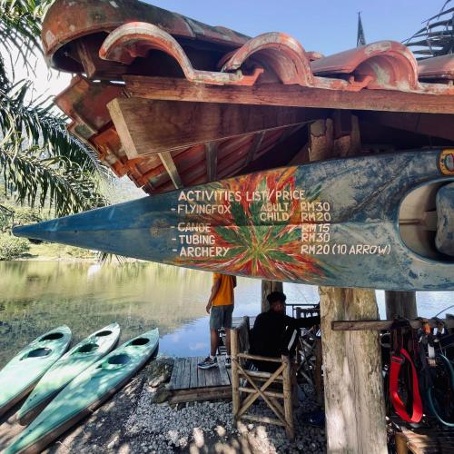a man sitting in a chair under a shack next to a river at Sahom Valley Resort - Agro & Eco Park in Kampar
