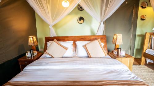 a bedroom with a bed with white sheets and two lamps at Lake Chahafi Resort in Kisoro