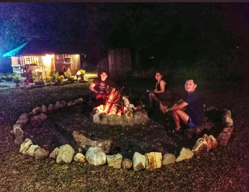 Trzech ludzi siedzących w nocy przy ognisku. w obiekcie Balai Consuelo Pamingwitan Campground w mieście Buliran