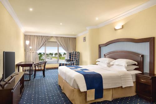 Howard Johnson Dammam Hotel في الدمام: غرفة فندقية فيها سرير ومكتب وتلفزيون