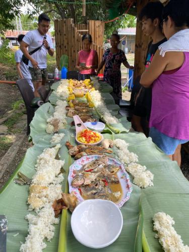 Długi stół z jedzeniem z ludźmi stojącymi wokół niego w obiekcie Balai Consuelo Pamingwitan Campground w mieście Buliran