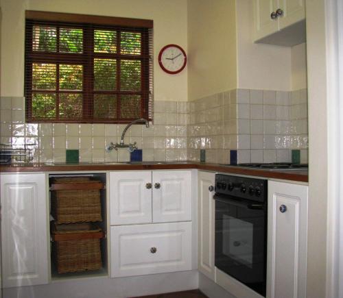 una cocina con armarios blancos y un reloj en la pared en Bakoven Cottage, en Ciudad del Cabo