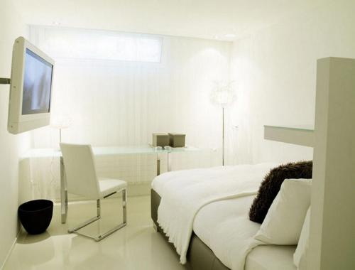 a white bedroom with a bed and a chair and a tv at VISIONAPARTMENTS Binzmühlestrasse 48 - contactless check-in in Zürich