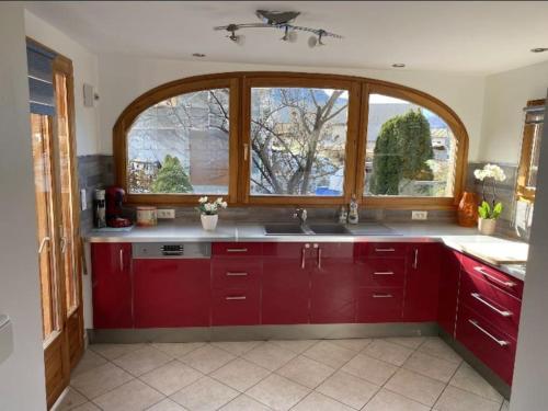 uma cozinha com armários vermelhos e uma grande janela em Bel Appartement modernisé avec terrasse. em Villar-Saint-Pancrace