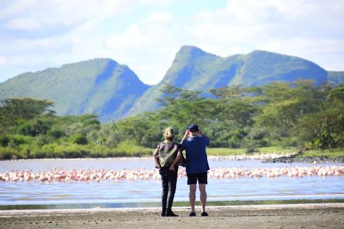 a man and woman standing on a beach with a flock of birds at Lake Elmenteita Serena Camp in Elmenteita