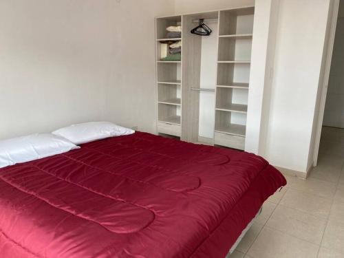 Una cama roja en una habitación blanca con estanterías en Departamento céntrico en Comodoro Rivadavia