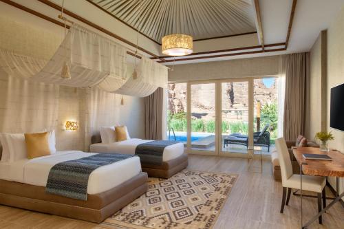 a hotel room with two beds and a desk and a television at Shaden Resort in AlUla