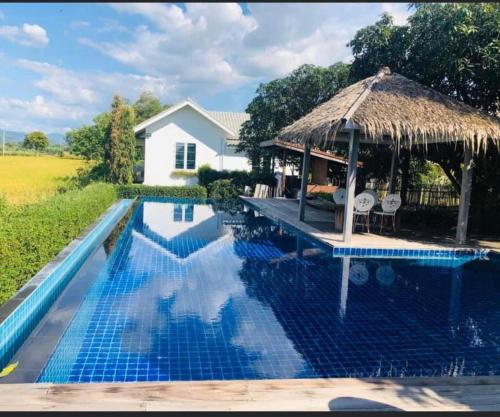 una piscina con sombrilla de paja y una casa en Mountain View Pool Villa en Nakhon Nayok