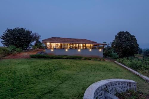 a large house with lights on a grass field at SaffronStays Anantham, Kamshet - pet-friendly lakefront villa with a huge verandah in Nethersole Dam