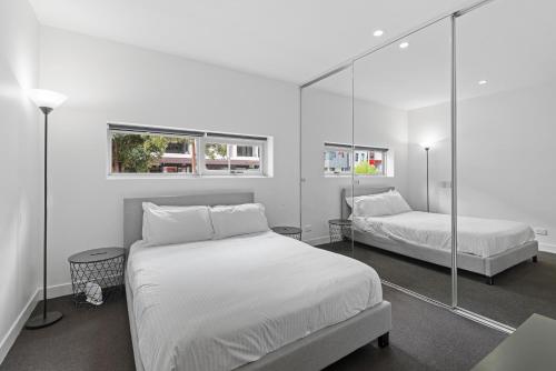 a white bedroom with two beds and a mirror at Newly Refurnished Beachside 1-Bedroom Apartment in Melbourne