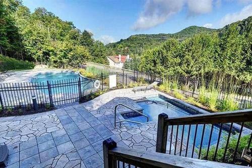a swimming pool on a patio with a fence at Condo entier, fully equiped pool and Spa only in summer in Mont-Tremblant