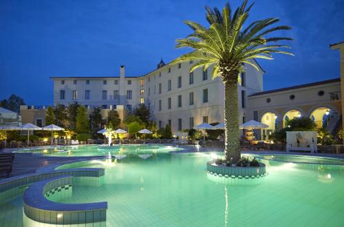 a large swimming pool with a palm tree in front of a building at Thermae Sylla Spa & Wellness Hotel in Loutra Edipsou