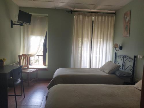 a bedroom with two beds and a desk and a window at Hostal La Cigueña in El Espinar
