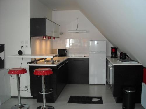 Les granvillaises في غرانفيل: مطبخ مع أجهزة بيضاء وسوداء وكراسي حمراء
