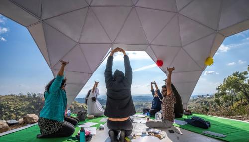 Hill Ventures - Swiss Glamping with Adventure Activities في دارامشالا: مجموعة من الناس يجلسون على طاولة ويدهم في السماء