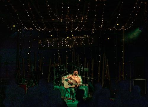 a man sitting in a chair playing a guitar at Hill Ventures Adventure Camp and Restaurant in Dharamshala