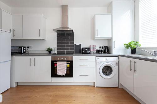 a kitchen with white cabinets and a washer and dryer at Spacious Comfortable house close to Etihad+parking in Manchester