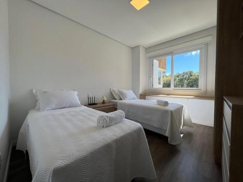 1 dormitorio blanco con 2 camas y ventana en Apartamentos Altos da Bela Vista by Achei Gramado, en Gramado