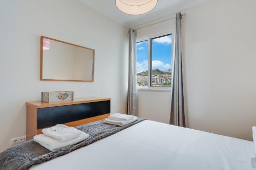 a white bedroom with a large bed and a window at Anje Apartamento in Funchal