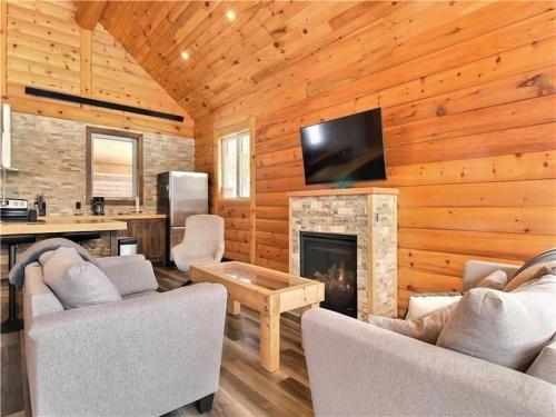 a living room with a fireplace and a tv at Le Billot- Chalet Rustic avec Spa in Saint-Philémon