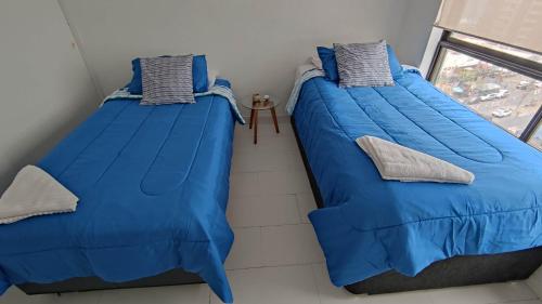 two beds in a room with blue sheets and a window at DEPTO SUITE II in Iquique