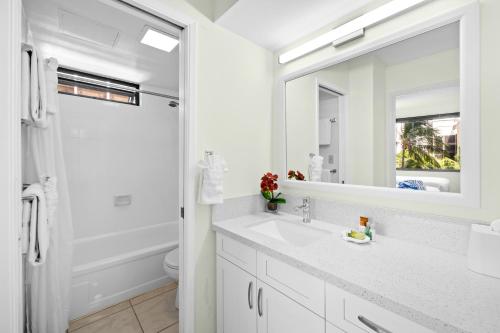 a white bathroom with a sink and a mirror at Waikiki Banyan Oasis with Partial Ocean View, 1-Block to Beach, Free Parking in Honolulu